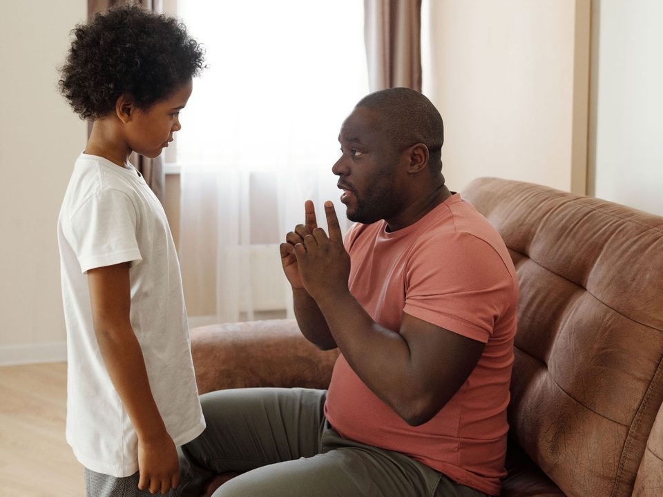 Father sitting on a couch, speaking with his young child who is standing beside him
