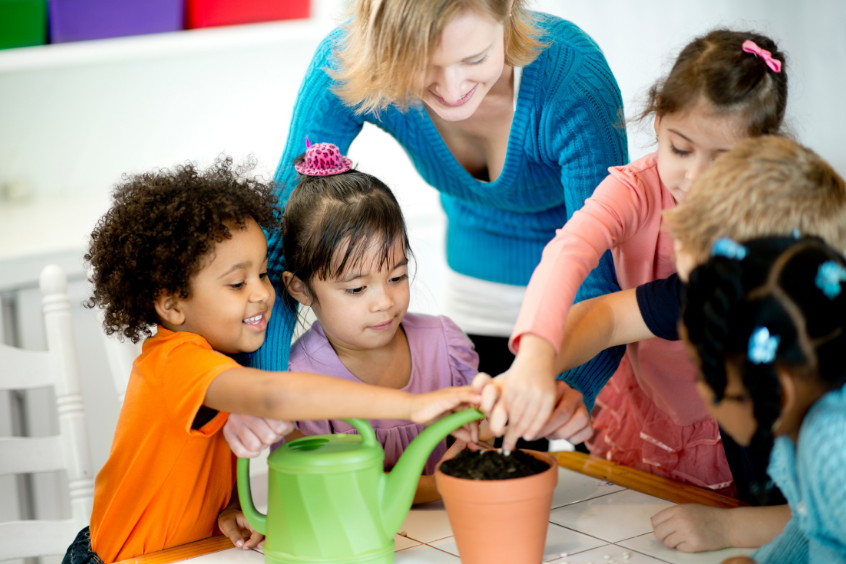 Diverse preschool children planting a seed together with their teacher 
